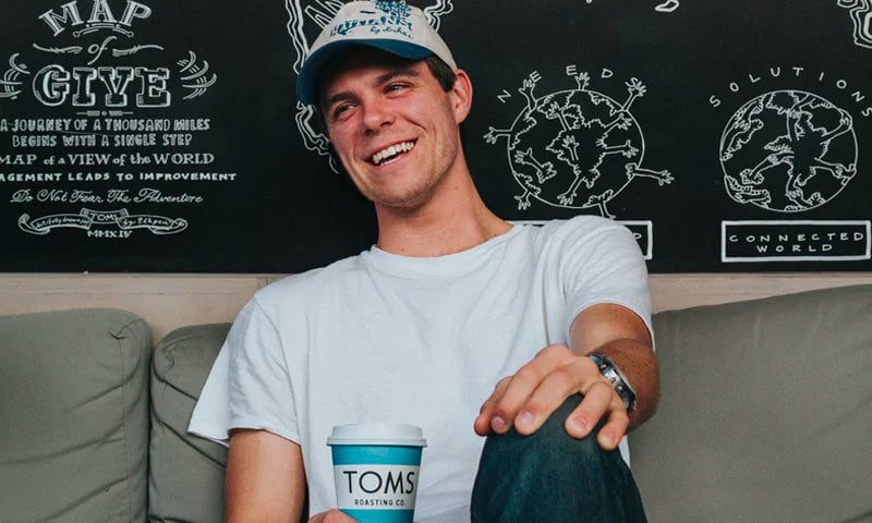 Smiling young man in white t-shirt and cap holding coffee cup, representing Nielseun customer